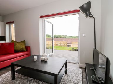 A living room with a red sofa pillows on a black coffee table and an open door leading to a garden at Egdon Heath in Nottington near Weymouth