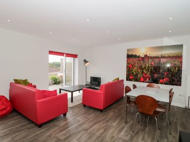 A living room with red sofas, a black coffee table, a flat screen TV, a dining table with wooden chairs, and a large wall art of a poppy field at Egdon Heath in Nottington near Weymouth