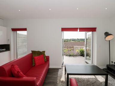 A living room with a red sofa and cushions a black table lamp and open double doors leading to a patio at Egdon Heath in Nottington near Weymouth