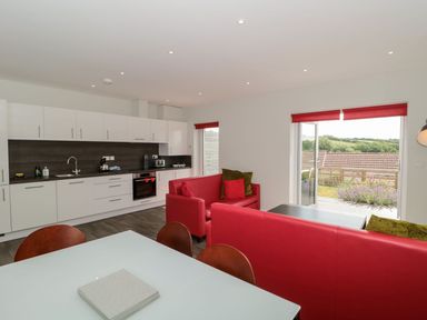 A kitchen and living area with white cabinets red sofas a white dining table and chairs and sliding doors opening to a garden at Egdon Heath in Nottington near Weymouth