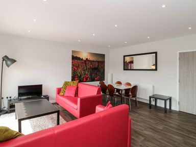A living room with red sofas a coffee table a dining table with chairs a floor lamp a television and wall art at Egdon Heath in Nottington near Weymouth
