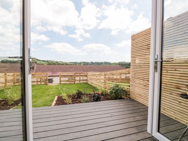 A garden with grass and plants viewed through open glass doors with wooden fencing on a deck at Egdon Heath in Nottington near Weymouth