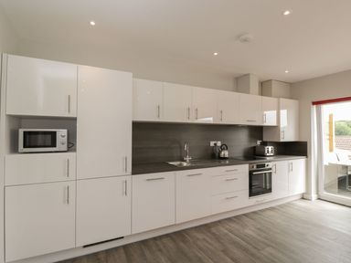 A kitchen with white cabinets a microwave kettle toaster oven and a glass door to a balcony at Egdon Heath in Nottington near Weymouth