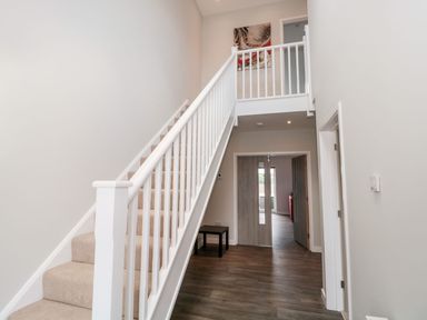 A hallway with carpeted stairs and wooden flooring with a small table and open doors at Egdon Heath in Nottington near Weymouth