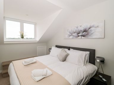 A bedroom with a double bed white bedding beige blanket a window with a potted plant bedside tables and a flower painting on the wall at Egdon Heath Nottington near Weymouth
