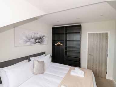 A bedroom with a bed white linens a gray headboard a black shelving unit with hangers and a wooden door at Egdon Heath Nottington near Weymouth