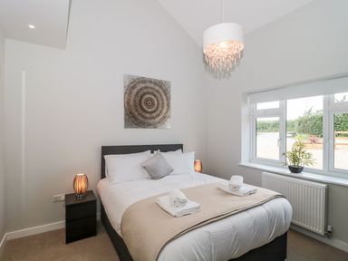 A bedroom with a bed bedside tables lamps window and wall art at Egdon Heath in Nottington near Weymouth