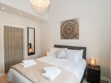 A bedroom with a bed bedside tables lamps a door and a wall mirror at Egdon Heath in Nottington near Weymouth