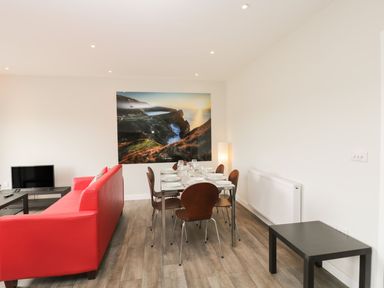 A dining area with a table set for six and a red sofa in a living room at Lulstead in Nottington near Weymouth
