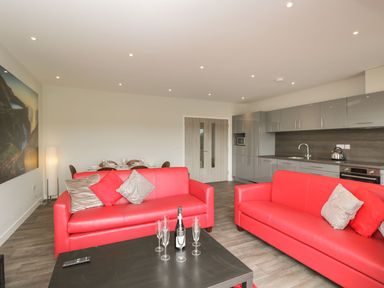 A living room with red sofas and a kitchen with grey cabinets at Lulstead in Nottington near Weymouth