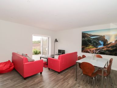 A living room with red sofas a black coffee table dining table with brown chairs and a large landscape photo on the wall at Lulstead in Nottington near Weymouth