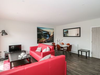 A living room with red sofas a black coffee table with tea set wooden chairs and a dining table at Lulstead in Nottington near Weymouth