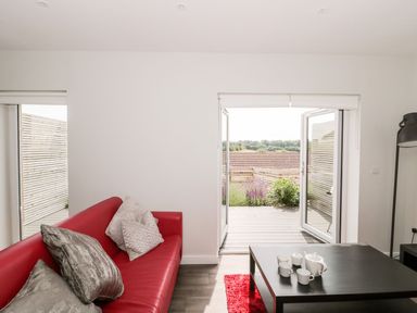 A living room with a red sofa and pillows and a black coffee table with a tea set near open doors leading to a patio at Lulstead in Nottington near Weymouth