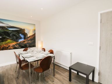 A dining area with a table set for six and wooden chairs a large landscape photo on the wall and a small black table at Lulstead in Nottington near Weymouth
