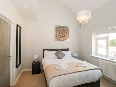 A bedroom with a double bed with pillows and folded towels bedside tables with lamps a wall mirror and a window at Lulstead in Nottington near Weymouth