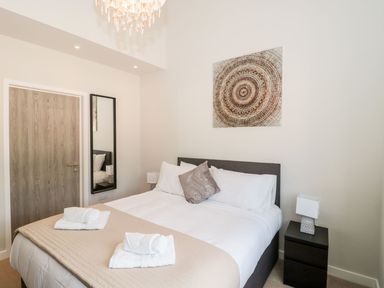 A bedroom with a double bed with towels on top a bedside table with a lamp a mirror and a wooden door at Lulstead in Nottington near Weymouth