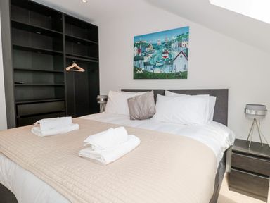 A bedroom with a bed towels on a beige bedspread a bedside table with a lamp an open shelving unit and a painting on the wall at Lulstead in Nottington near Weymouth