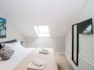 A bedroom with a bed with folded towels on a quilt a skylight window a wall-mounted TV and a standing mirror at Lulstead in Nottington near Weymouth