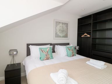 A bedroom with a double bed with rabbit pillows bedside tables with lamps and an open wardrobe at Lulstead in Nottington near Weymouth