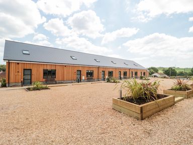 A row of wooden lodges with gravel in front and raised planters in a rural setting at Overcombe Mill in Nottington near Weymouth
