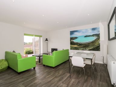 A living room with green sofas a coffee table a dining table with white chairs and a large landscape photograph on the wall at Overcombe Mill in Nottington near Weymouth