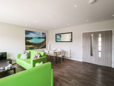 A living room with green sofas white chairs dining table and coastal photograph on wall at Overcombe Mill in Nottington near Weymouth