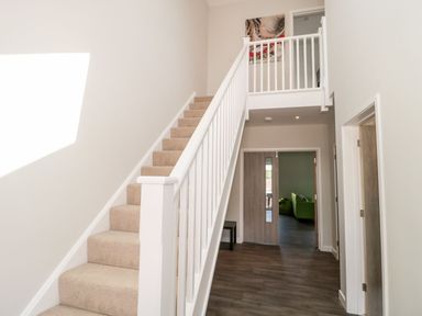 A hallway with carpeted stairs and wooden floor leading to a room with a green sofa at Overcombe Mill in Nottington near Weymouth