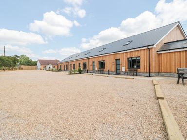 A long wooden building with multiple black doors and windows beside a gravel area at Corvesgate in Nottington near Weymouth
