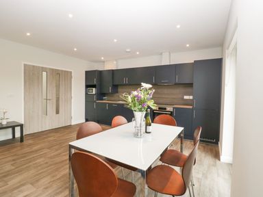 A kitchen with black cabinets a white table with flowers and six brown chairs at Dirdale in Weymouth