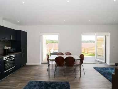 A dining area with a table and six chairs next to a kitchen with black cabinets at Dirdale in Weymouth
