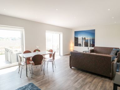 A dining area with table and chairs next to a living room with sofas and a large photo on the wall at Dirdale in Weymouth