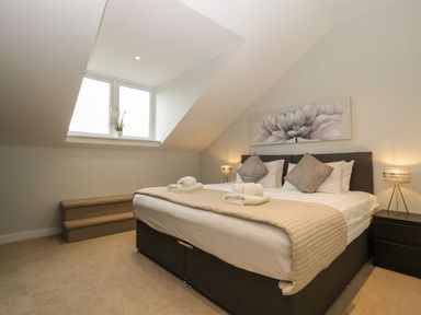 A bedroom with a double bed two bedside tables with lamps a small staircase and a window with a plant at Dirdale in Weymouth