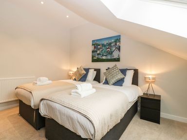 A bedroom with two single beds side by side with beige bedspreads and pillows a nightstand with a lamp and a painting on the wall at Dirdale in Weymouth