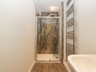 A bathroom with a walk in shower with glass doors a chrome towel rack and a white bathtub at Dirdale in Weymouth