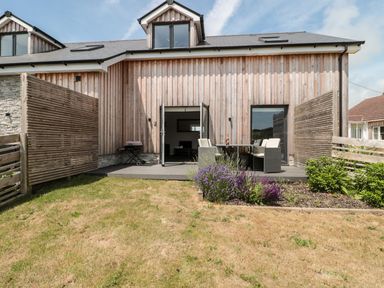 A backyard with wooden deck table and chairs and a small lawn at Dirdale in Weymouth