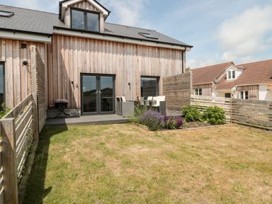A backyard with a lawn a wooden fence a patio table with chairs and a barbecue outside a wooden house at Dirdale in Weymouth