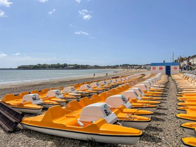 Rows of yellow and white pedal boats on a pebbled beach near the sea at Dirdale in Weymouth