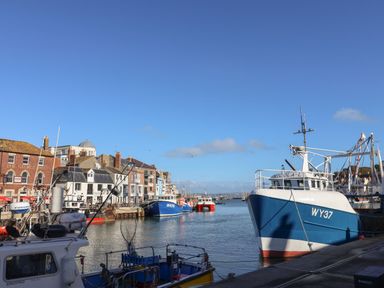 A harbor with fishing boats docked along the water and buildings in the background at Dirdale in Weymouth