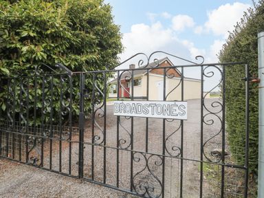 A black iron gate with a Broadstones sign and a cream house with red door behind it at Broadstones in Bridport