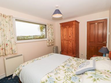 A bedroom with a double bed floral bedding wooden wardrobe window with curtains and a wooden door at Broadstones in Bridport