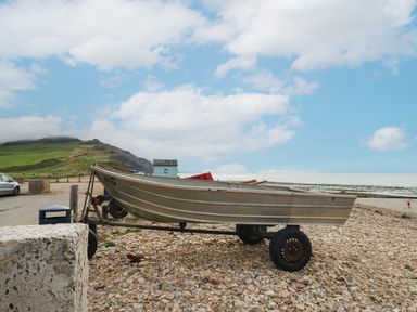 A metal boat on a trailer on a pebble beach with a hill and cloudy sky in the background at Broadstones in Bridport