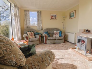A sitting room with patterned sofas, a wood burning stove, curtains and framed pictures at Broadstones in Bridport