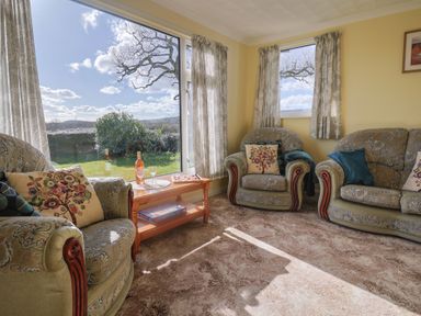 A living room with upholstered armchairs and a sofa around a wooden coffee table with a bottle and glasses at Broadstones in Bridport