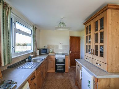 A kitchen with wooden cabinets a sink a microwave an oven and a refrigerator at Broadstones in Bridport