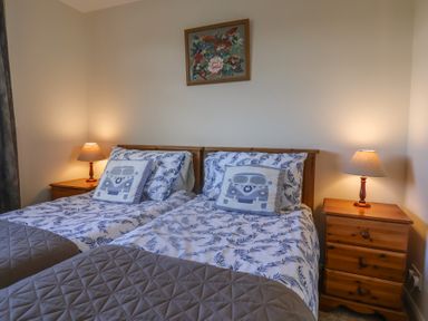 A bedroom with two single beds with patterned bedspreads and pillows and two bedside tables with lamps at Broadstones in Bridport