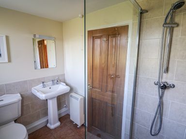 A bathroom with a toilet sink mirror shower area and wooden door at Broadstones in Bridport