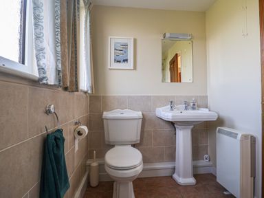 A bathroom with a toilet sink mirror towel rail and window at Broadstones in Bridport