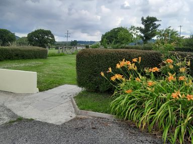 A garden with orange flowers a trimmed hedge concrete path and green fields in the background at Broadstones Bridport