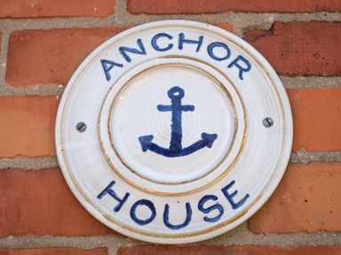 A round ceramic sign mounted on a brick wall with an anchor symbol and the words Anchor House in Weymouth