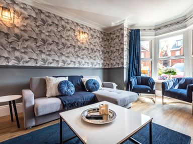 A living room with a grey sectional sofa and blue cushions blue armchairs and a white coffee table at Anchor House in Weymouth